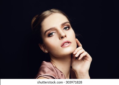 Portrait of young beautiful woman with light makeup and blue eyes touching her face. Dark background. Wearing pearls earrings.