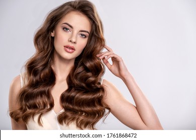 Portrait of a young beautiful woman with a long hair. Attractive fashion model with  brown hair - isolated on white background. Young girl with wavy hair looks to the camera.