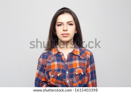 Portrait young beautiful woman not smiling in plaid shirt isolated on white-gray background. Girl with minimal natural make-up on her face. The photo is not retouched with natural defects on the skin.