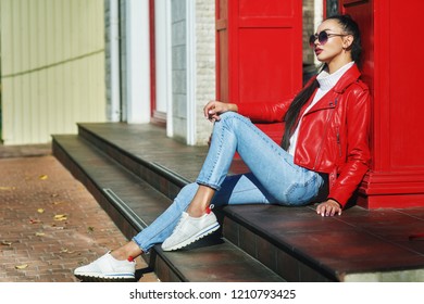 Portrait Of A Young Beautiful Woman On A City Street . The Model Is Dressed In A Stylish Leather Biker Jacket, Turtleneck, Blue Jeans