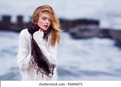 Portrait of young beautiful woman outdoor - standing on seaside and holding waving fabric scarf in her arms on wind
