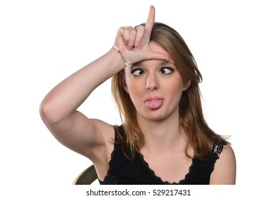 Portrait Of Young Beautiful Woman Peeping At The Camera Making Funny Face And Showing Loser Sign. Isolated On White