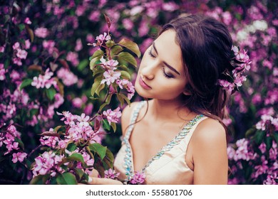 Portrait of young beautiful woman posing among blooming apple trees