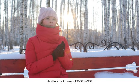 Portrait young beautiful woman in red warm jacket sits waiting on bench in Park on beautiful frosty Sunny day.
