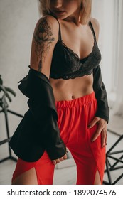 Portrait Of Young Beautiful Woman In Red Pants With Strut, Top, Bra And Black Jacket At Home Make A Belly Vacuum.  White Walls, Background, Fashion. Healthy Lifestyle, Sports, Care.