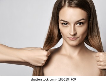 Portrait of young beautiful woman with silky long straight hair looking at camera and holding her strong healthy hair in hands over grey background. Hairstyle, hairsalon, hairdresser, fashion concept