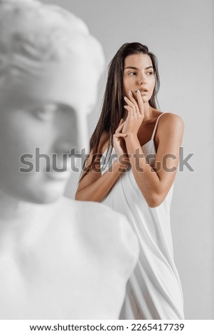 Portrait of young beautiful woman standing near gypsum sculpture Venus face