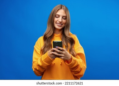 Portrait of young beautiful woman texting on the phone against blue background - Shutterstock ID 2211172621