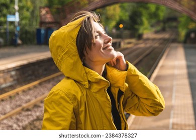 Portrait of young beautiful woman  traveler  wearing yellow raincoat outside in autumn scenery waiting for a metro train, small trips escapes from city at the weekend concept