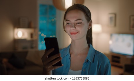 Portrait of Young Beautiful Woman Using Smartphone, Browsing in Internet, Checking Social Networks and Using Smart Home Application while Standing At Home. Cozy Evening. - Powered by Shutterstock