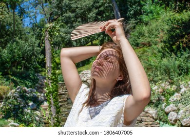 Portrait Of Young Beautiful Woman  Using Hand Fan In Very Hot Summer Day Outdoors. Lady Cooling Herself. Suffering From High Temperature Outside.