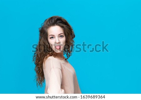 Portrait of a young beautiful woman wearing sweatshirt shows tongue isolated over blue background