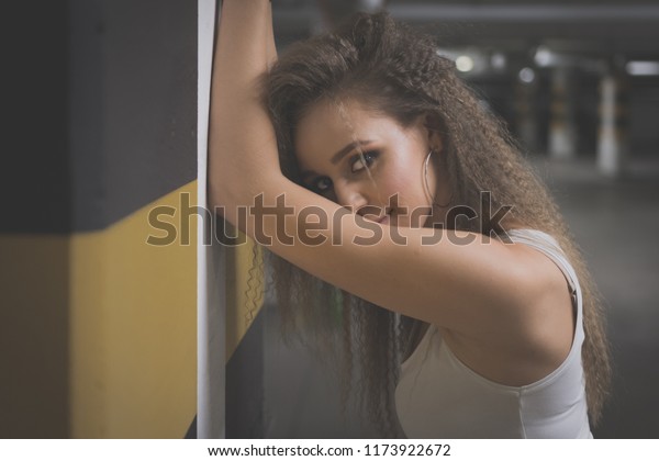 Portrait of young\
beautiful woman wearing white tank shirt and blue jeans with long\
hair at underground\
garage