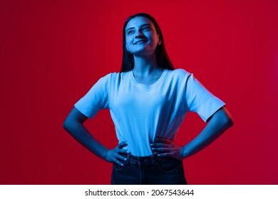 Portrait Of Young Beautiful Woman In White T-shirt Smiling And Looking Up Isolated Over Red Background In Neon Lights. Concept Of Feelings, Youth, Fashion, Facial Expression, Emotions, Lifestyle, Ad