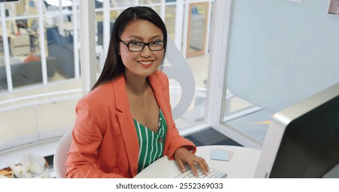 Portrait of a young biracial female business creative working in a modern office, using a computer, smiling to camera - Powered by Shutterstock