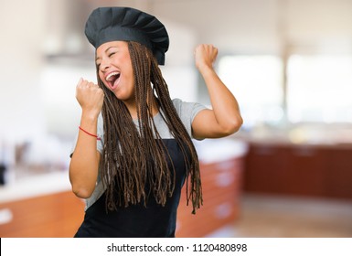 Portrait Of A Young Black Baker Woman Very Happy And Excited, Raising Arms, Celebrating A Victory Or Success, Winning The Lottery