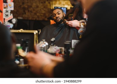 Portrait Of Young Black Man Being Trimmed With Professional Electric Clipper Machine In Barbershop.Male Beauty Treatment Concept. Young African Guy Getting New Haircut In Barber Salon