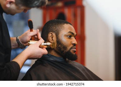 Portrait Of Young Black Man Being Trimmed With Professional Electric Clipper Machine In Barbershop.Male Beauty Treatment Concept. Young African Guy Getting New Haircut In Barber Salon