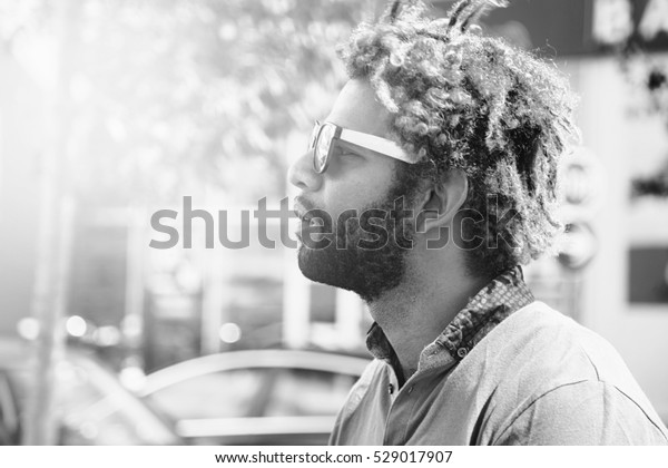 Portrait of young black man with\
dread locks wearing sunglasses. Black and white effect\
applied.