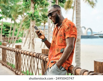 Portrait of a young black man guy taking a selfie with a smartphone mobile phone , having fun and laughing, walking close to beach in tourist  holiday destination - Powered by Shutterstock