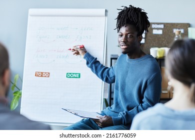 Portrait Of Young Black Man Teaching English Class In Office To Group Of People And Pointing At Whiteboard With Grammar Rules