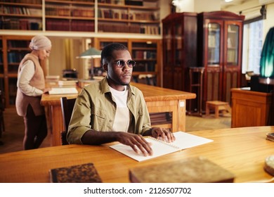 Portrait of young black man with vision impairment reading book in braille at table in college library - Powered by Shutterstock