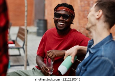 Portrait Of Young Black Man Wearing Bandana And Laughing Happily While Enjoying Chat With Friends Outdoors