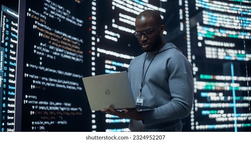 Portrait of Young Black Man Working on Laptop, Looking at Big Digital Screen Displaying Back-end Code Lines. Professional Programmer Developing a Big Data Interface Software Project Concept. - Powered by Shutterstock