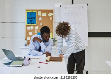 Portrait Of Young Black Teacher Helping Boy With Task Or Grading Homework In School Classroom