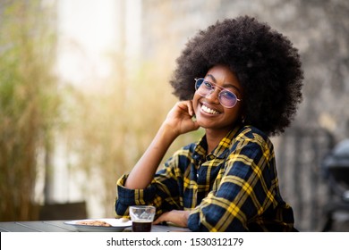 Portrait Of Young Black Woman With Afro Hair And Glasses Sitting Outside And Smiling