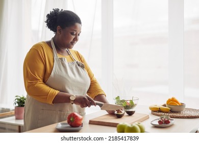 Portrait Of Young Black Woman Cutting Avocado While Making Salad In Sunlit Kitchen, Copy Space