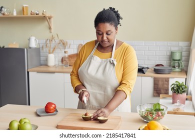 Portrait Of Young Black Woman Cutting Avocado While Cooking Healthy Meal In Kitchen, Copy Space