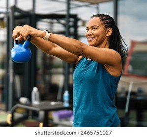 Portrait of a young black woman  exercising in a gym, lifting weights, kettlebell equipment, healthy lifestyle and strength exercise at fitness club concepts - Powered by Shutterstock