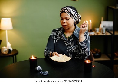 Portrait Of Young Black Woman Reading Tarot Cards In Fortune Tellers Shop Lit By Candles, Copy Space