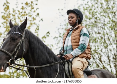 Portrait Of Young Black Woman Riding Horse Outdoors And Wearing Protective Helmet, Copy Space