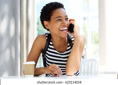 Portrait of young black woman sitting at cafe talking on mobile phone