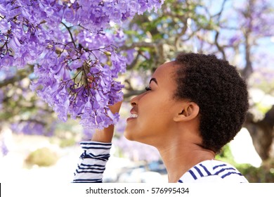 Portrait Of Young Black Woman Smelling Flowers On Tree