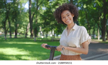 Portrait of young black woman smiling, standing with electric scooter in park - Powered by Shutterstock