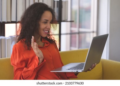 Portrait Of A Young Black Woman Wearing Orange Shirt Smiling And Using Laptop For Video Call On Sofa At Home. Business Woman And Freelance Work From Home In Spreading Of Coronavirus Covid-19.