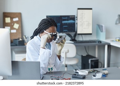 Portrait of young black woman wearing magnifying visor and inspecting hardware part in engineering laboratory - Powered by Shutterstock