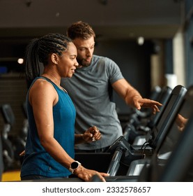 Portrait of a young black woman and white man coach or trainer exercising in a gym, running using  thereadmill machine equipment, healthy lifestyle and cardio exercise at fitness club concepts - Powered by Shutterstock