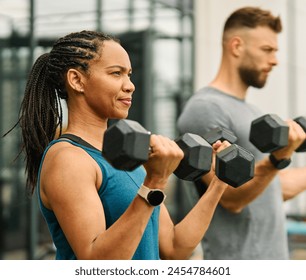 Portrait of a young black woman and white man coach or trainer exercising in a gym, lifting weights,  dumbbell equipment, healthy lifestyle and strength exercise at fitness club concepts - Powered by Shutterstock