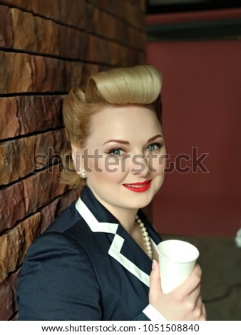 Portrait of young blond lady with craft cup. Pin-up styled girl on brick wall background. Happy smiled  woman with blonde curves