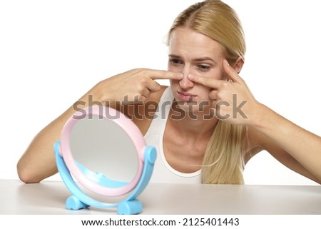 portrait of a young blond woman touches her nose in the mirror on a white background
