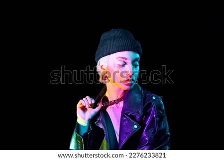 Portrait of young blonde girl with neon holographic colors on body posing over dark background in blue neon lights. Concept of art, modern style, cyberpunk, futurism and creativity