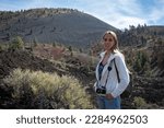 Portrait of a young blonde girl with a photo camera in the natural landscape of lava lake at sunset crater volcano