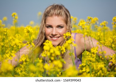 Portrait of young blonde woman in Canola field blossom, looking at camera