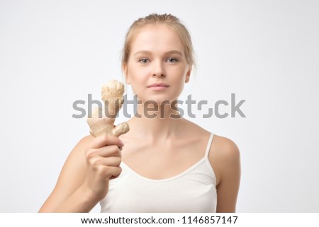 Portrait of young blonde woman holding raw ginger root. Healthy food for weight loss