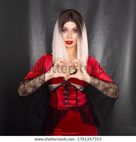Portrait of a young blonde woman in a red vampire costume on a black background in the studio