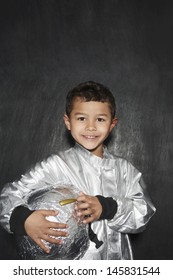 Portrait Of Young Boy In Astronaut Costume Holding Helmet Against Black Background